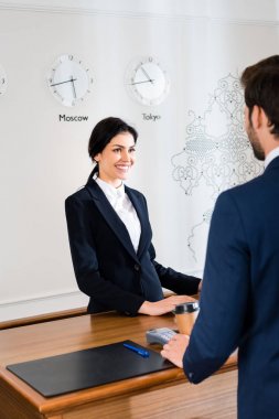 cropped view of man standing near happy receptionist in hotel  clipart