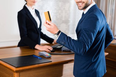 resepsiyonist yakınında kredi kartı tutan neşeli işadamı kırpılmış görünümü 