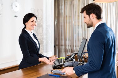 selective focus of happy receptionist gesturing near handsome man with credit card  clipart