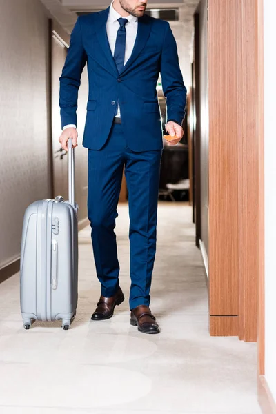 スーツケースを持って立っている間 ホテルのカードを持っているあごひげのビジネスマンのトリミングビュー — ストック写真