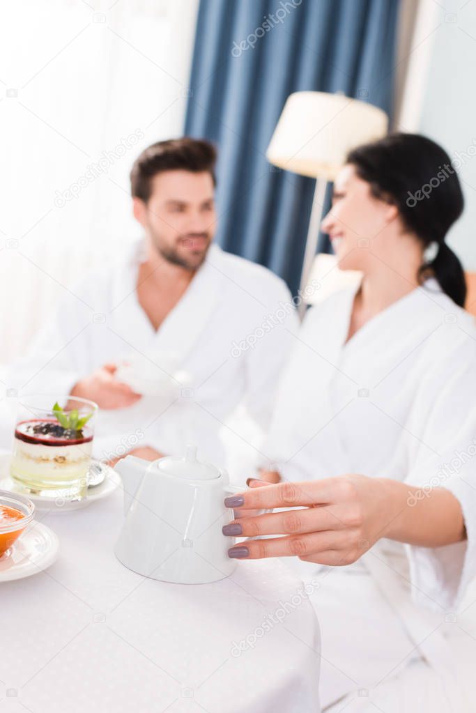 selective focus of woman holding teapot and looking at man 