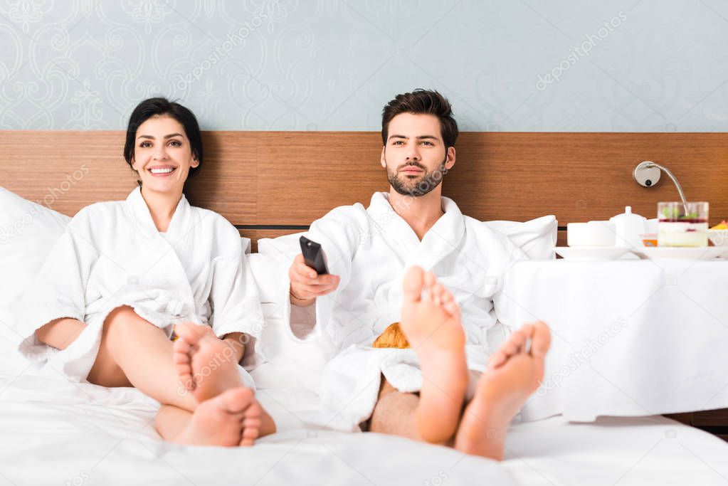 selective focus of cheerful man holding remote controller near attractive woman in hotel room 