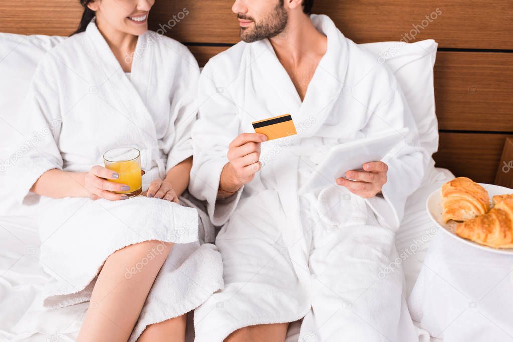 cropped view of man with credit card using digital tablet near happy woman