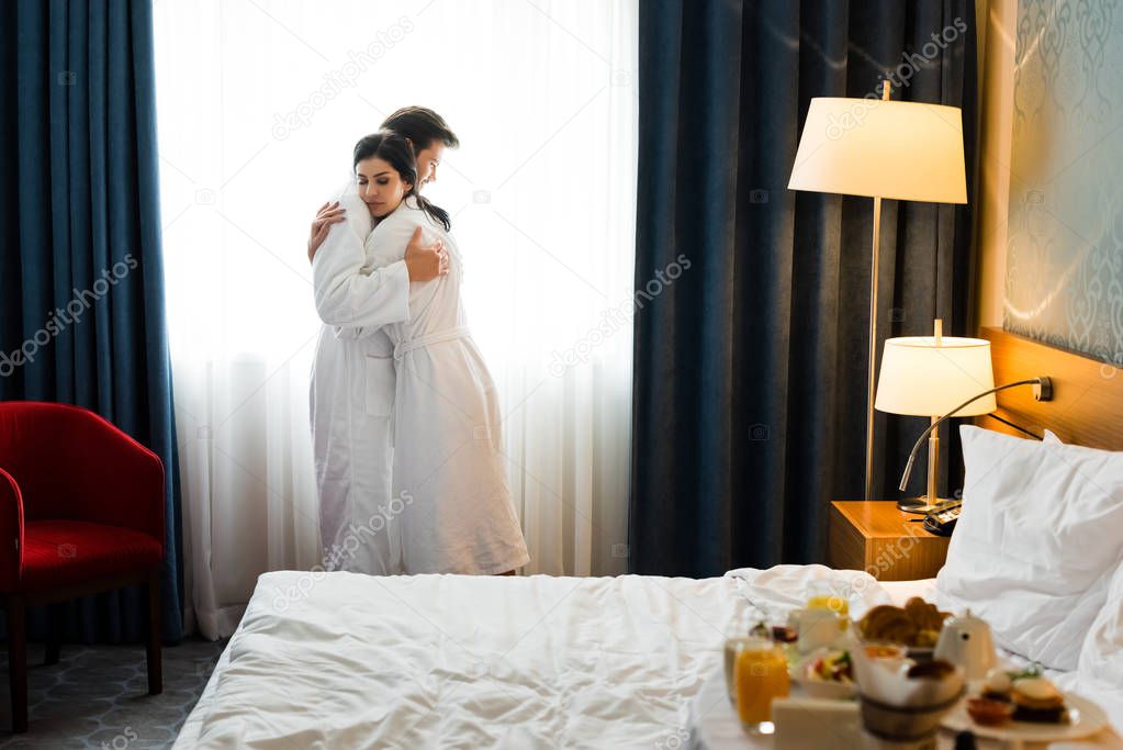 selective focus of handsome man and attractive brunette woman hugging in hotel room 
