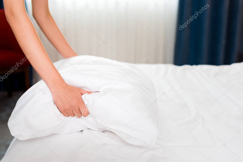 cropped view of housemaid holding white pillow in hotel room 