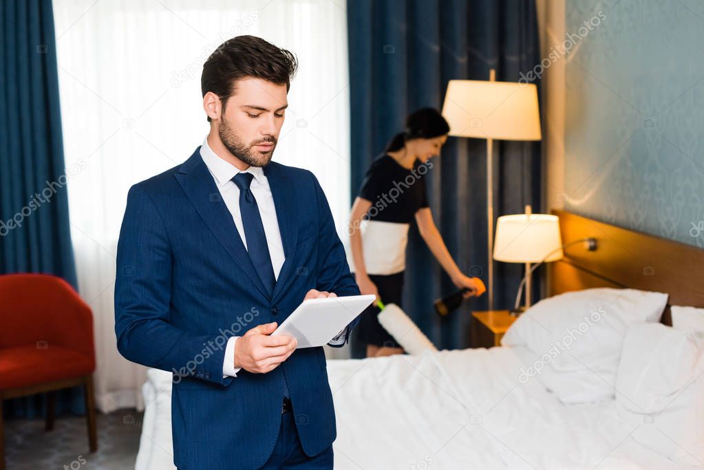 selective focus of handsome man using digital tablet near maid in hotel room 