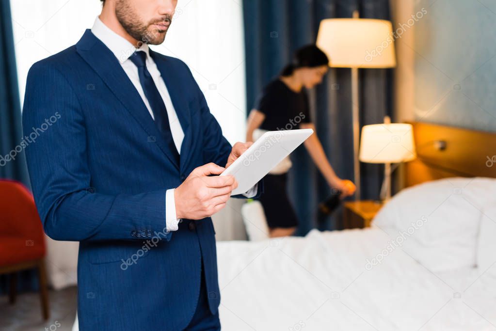 cropped view of man using digital tablet near maid in hotel room 