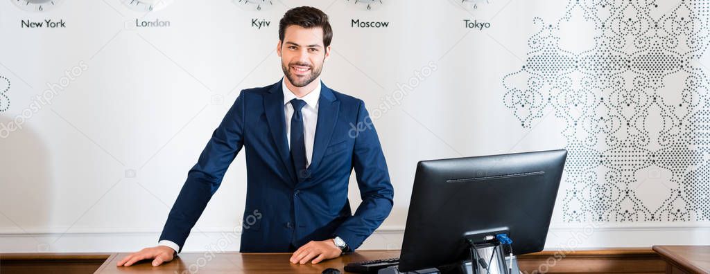 panoramic shot of happy receptionist standing at reception desk in hotel 