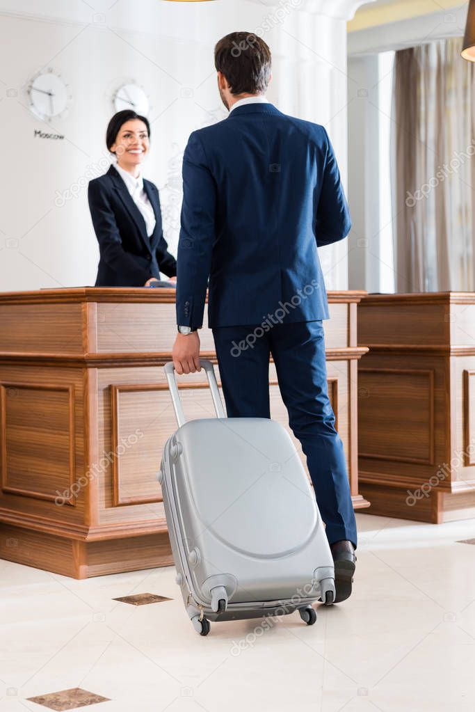 selective focus of businessman with suitcase standing near beautiful receptionist 