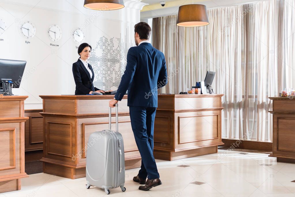 attractive receptionist looking at businessman with luggage 