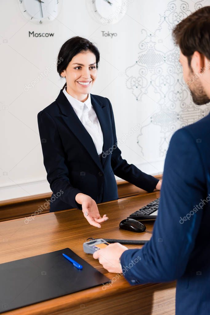 cropped view of man paying while holding credit card near happy receptionist in hotel 