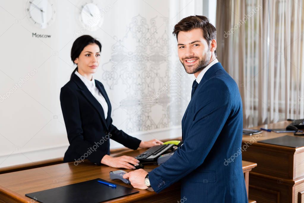 selective focus of happy businessman holding credit card near serious receptionist 