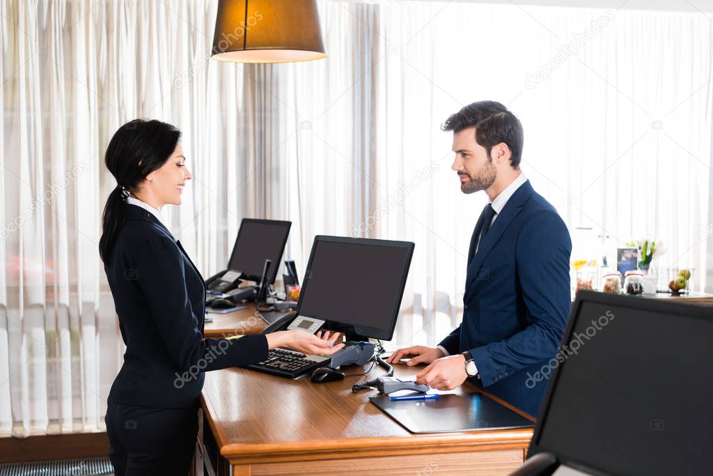 happy receptionist gesturing near handsome man with credit card 