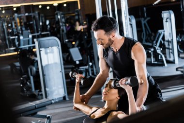 genç atletik kadın seçici odak spor salonunda eğitmen yakın dumbbells ile çalışma 
