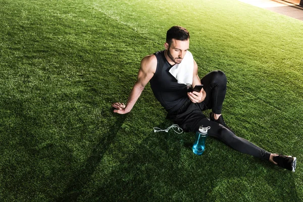 Hombre Atlético Guapo Usando Teléfono Inteligente Mientras Está Sentado Hierba — Foto de Stock