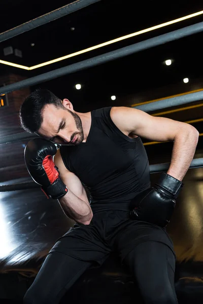 低角度视图疲惫的胡子男子在黑色拳击手套触摸头部在健身房 — 图库照片