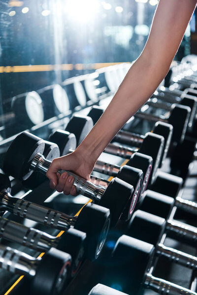 cropped view of sportswoman taking dumbbell in gym 