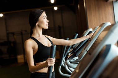 selective focus of attractive woman in sportswear working out on exercising bike  clipart