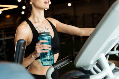 egzersiz bisikleti üzerinde çalışırken spor şişesi tutan atletik kadın kırpılmış görünümü 