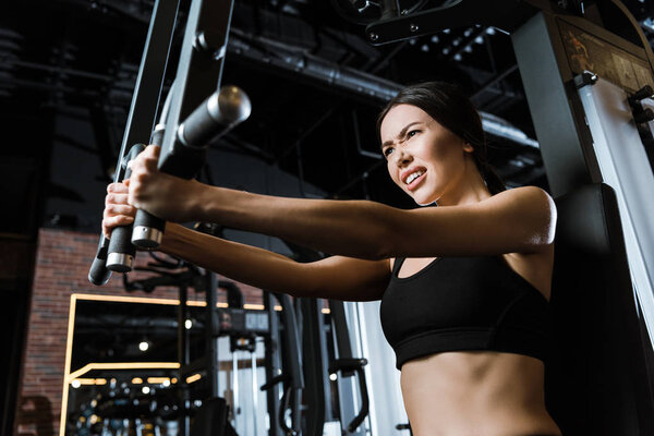 low angle view of strong sportswoman in sportswear exercising on training apparatus in gym 