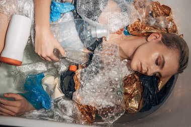 top view of young woman posing in bathtub with plastic waste, eco concept clipart