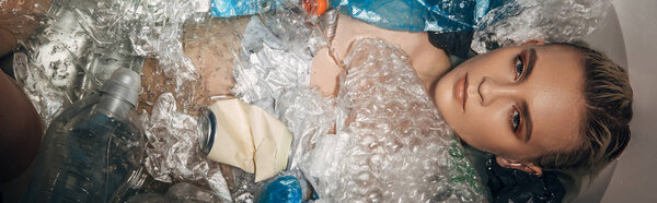 panoramic shot of beautiful woman among plastic waste in bathtub, eco concept