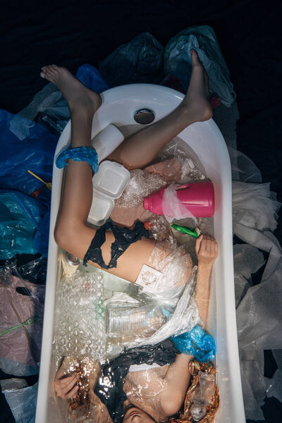 top view of young woman lying in bathtub among plastic trash, environmental pollution concept