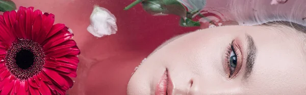 色とりどりのピンクの水と花で浴槽に横たわっている美しい若い女性のトップビュー パノラマショット — ストック写真