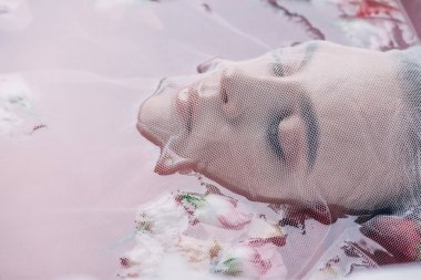 gül yaprakları ile pembe suda beyaz örgü bez ile kaplı güzel kadın yakından görünümü 