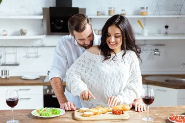 mutlu çift doğrama tahtasında ekmek keserken mutfakta birlikte duran