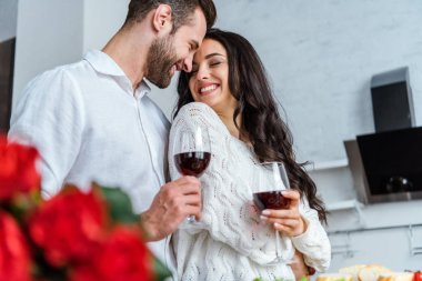 selective focus of happy couple holding glasses with red wine and looking at each other clipart