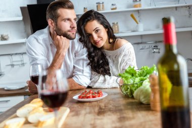young couple near wooden table with red wine, cherry tomatoes, bread and salad