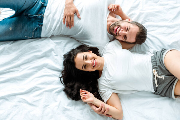 top view of happy smiling couple lying together in bed 