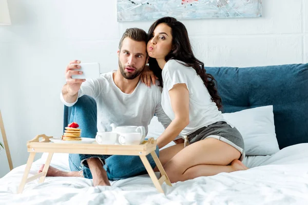 Funny Couple Grimacing Taking Selfie Smartphone Wooden Tray Breakfast Bed — Stock Photo, Image