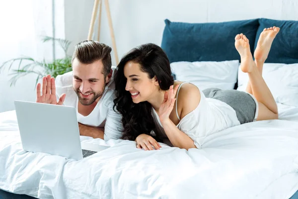 Feliz Casal Acenando Mãos Durante Vídeo Chat Laptop Deitado Cama — Fotografia de Stock