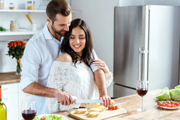 Feliz Casal Juntos Cozinha Enquanto Homem Cortando Pão Tábua Cortar — Fotografia de Stock