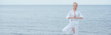 panoramic shot of young blonde woman with closed eyes practicing yoga  clipart