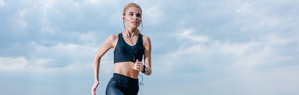 panoramic shot of sportive blonde woman running and listening music in earphones 