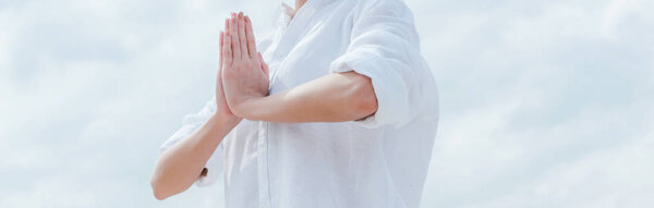 panoramic shot of young woman with praying hands near sky