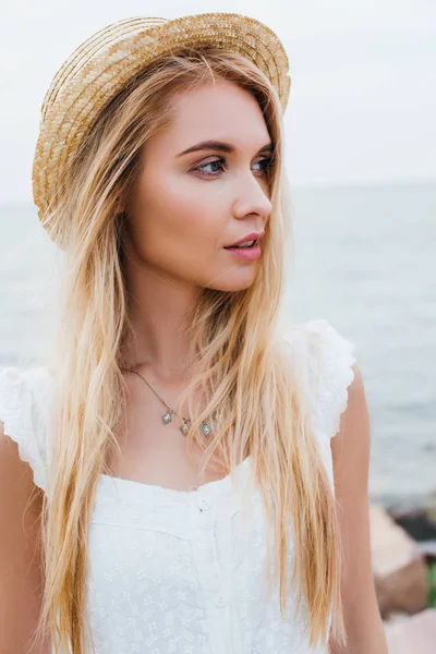 海の近くに白いドレスとわら帽子を着た魅力的な若い女性 — ストック写真