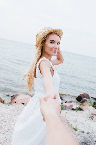 cropped view of man holding hands with happy blonde woman in straw hat 