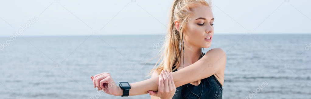panoramic shot of beautiful athletic girl stretching and listening music near sea 