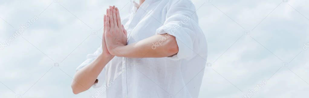 panoramic shot of young woman with praying hands near sky