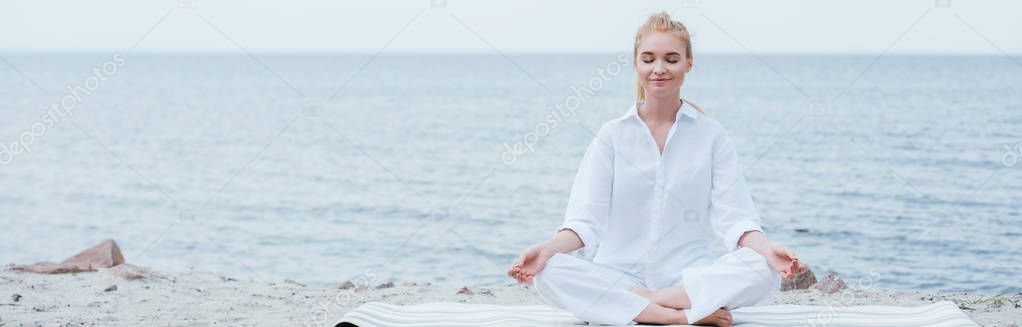 panoramic shot of peaceful blonde young woman with closed eyes practicing yoga near river 