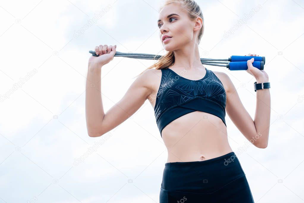 low angle view of young woman in sportswear standing and holding jump rope 