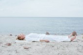 přitažlivá blondýnka s zavřenýma očima, když leží na rohoži u moře 