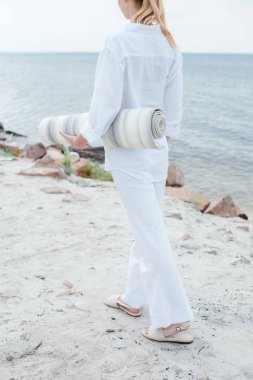 cropped view of young woman holding yoga mat and standing near sea  clipart