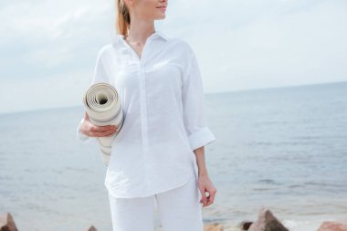 cropped view of happy young woman standing near sea and holding yoga mat  clipart