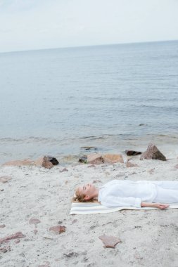 deniz kenarında yoga mat yatarken meditasyon kapalı gözleri ile güzel sarışın kadın 