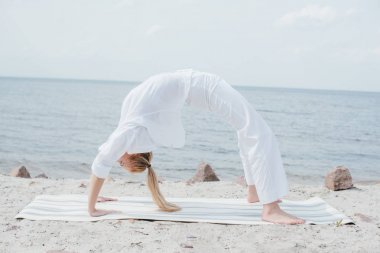 young blonde woman practicing yoga on yoga mat near sea  clipart